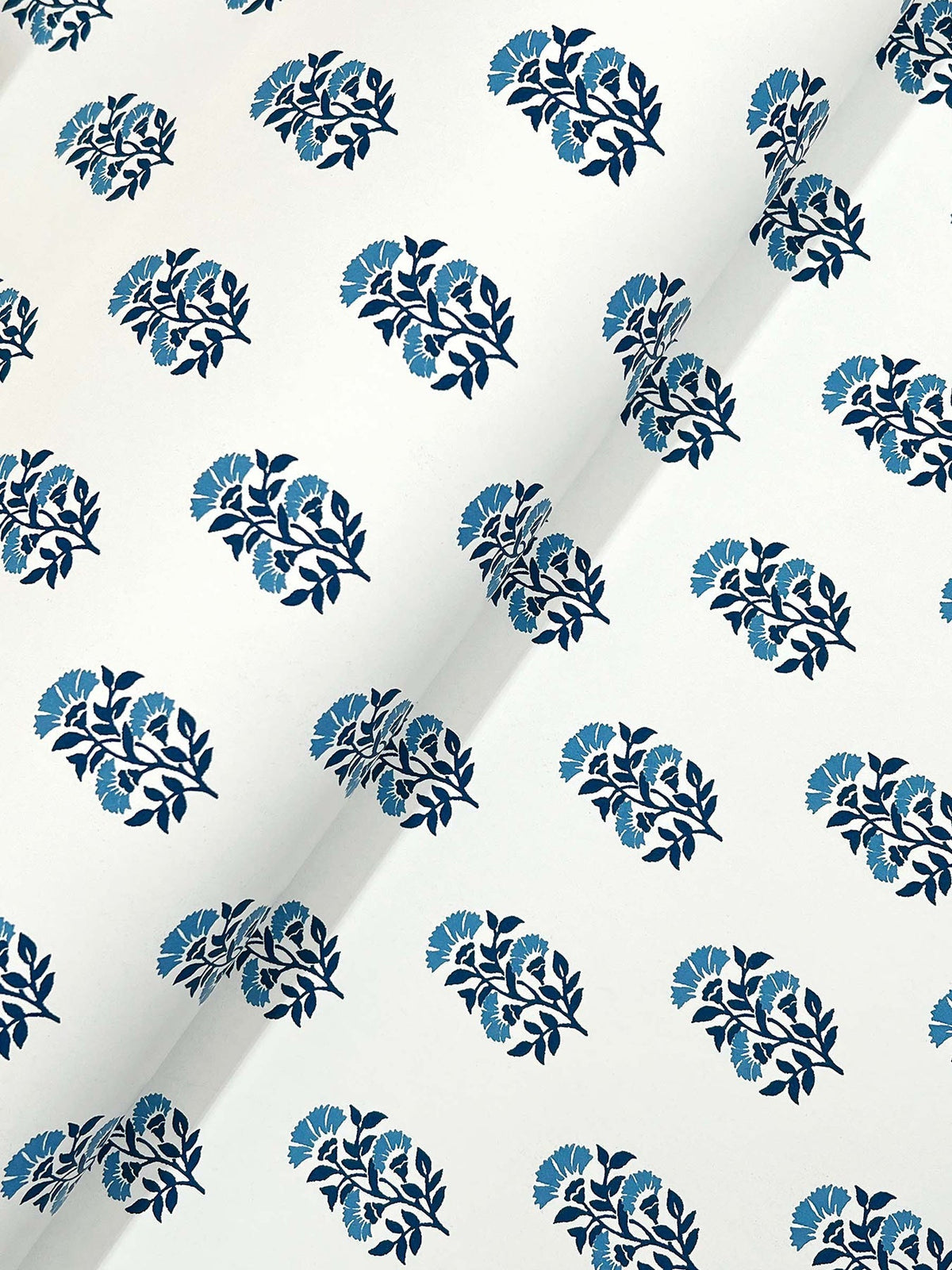 Sylvie Floral Wallpaper by York Wallcoverings showcases a repeating blue floral pattern of stylized flowers and leaves on a white background. The slightly curved paper creates subtle shadows across the surface.