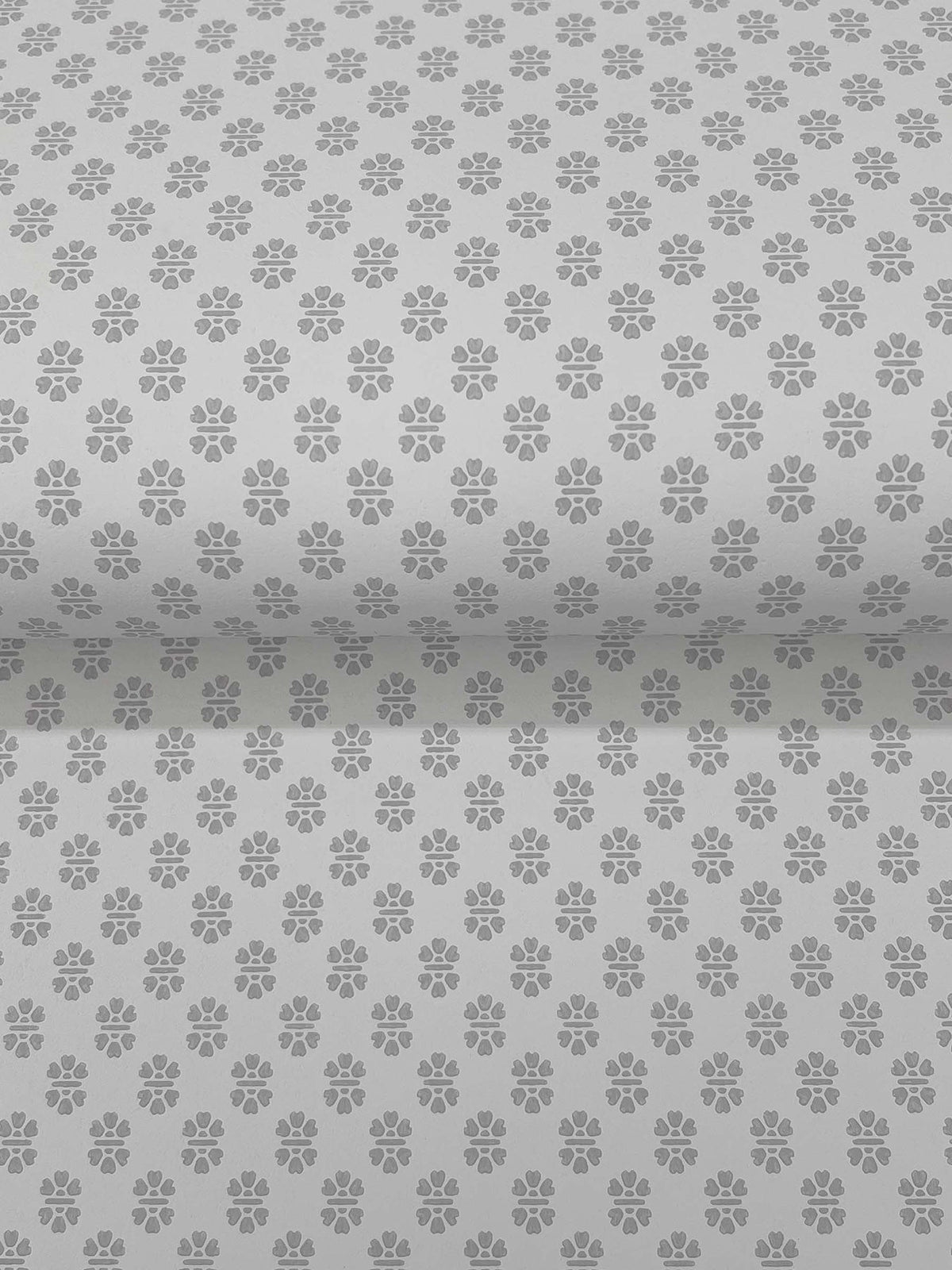 Brioni Floral Stamp Wallpaper by York Wallcoverings features a repeating pattern stamped across a gray background. The wallpaper is shown unrolled, displaying the uniform floral design across its entire surface.