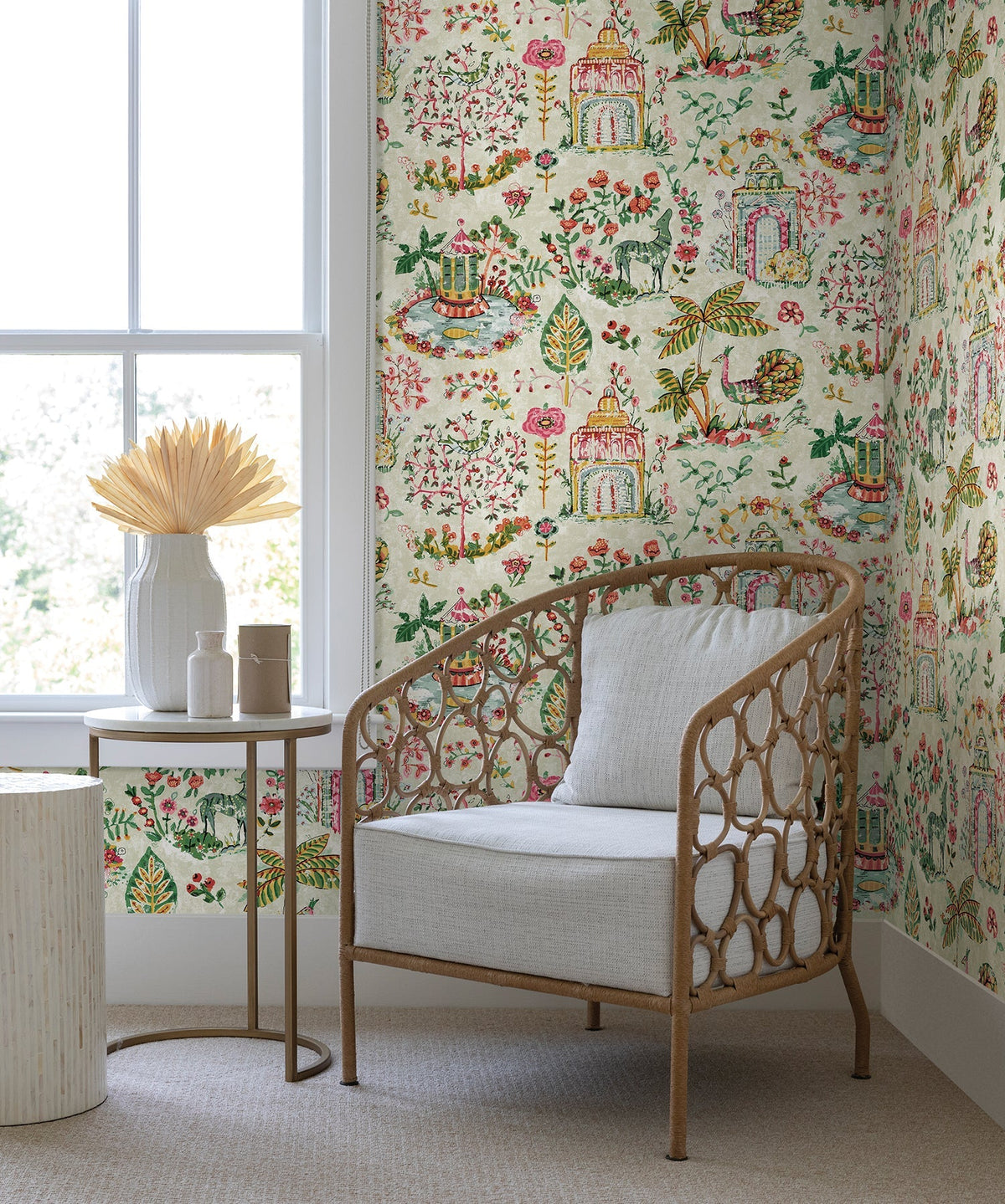 A cozy chair with a light cushion sits by a small table adorned with vases and dried flowers, set against York Wallcoverings’ Parc Garden Dreams Wallpaper near a large window.