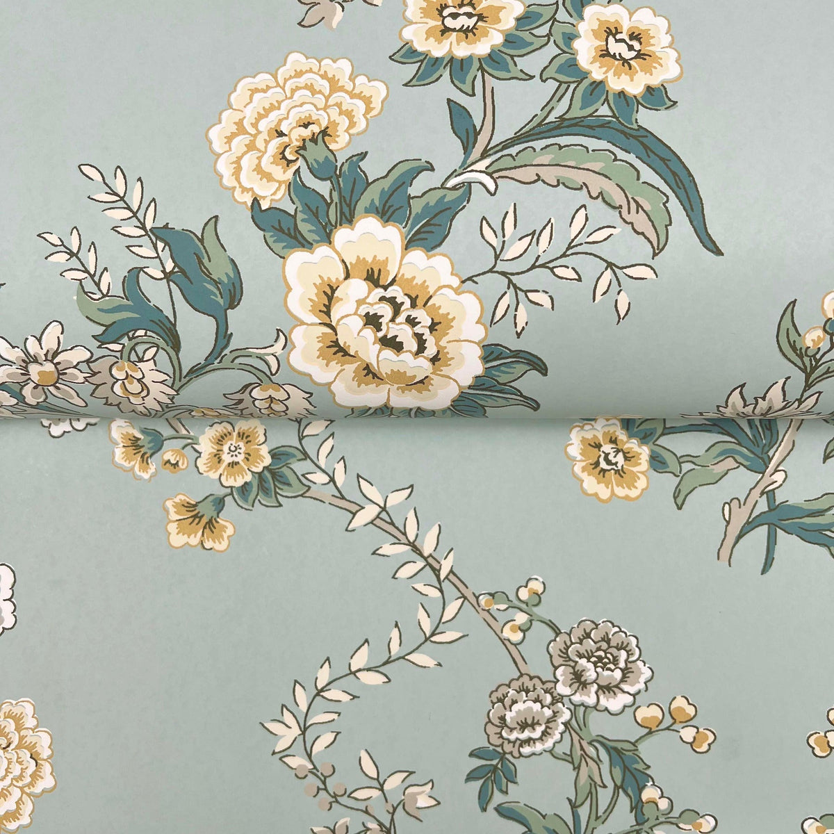 Partially unrolled, the Genevieve Floral Trail Wallpaper by York Wallcoverings features a pale green background adorned with a vintage-inspired floral pattern of yellow, cream, and white flowers intertwined with dark green leaves and vines.