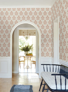 A hallway featuring York Wallcoverings’ Souci Marigolds Wallpaper, an arched doorway, a black bench with cushion, a blue rug, and a view into a bright dining area with a round white table, wooden chairs, and a vase of flowers.
