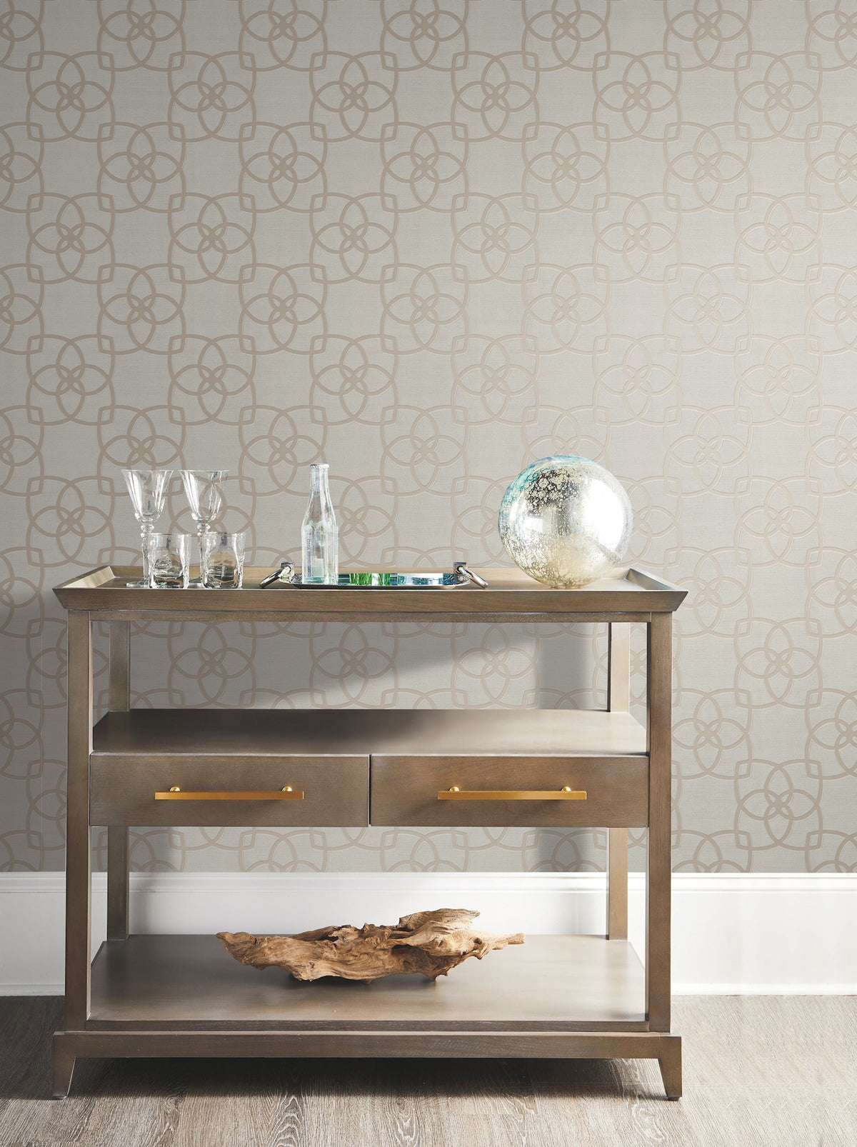 A wooden bar cart with glasses, a bottle, a tray, and a decorative globe sits against a wall adorned with Serendipity Wallpaper by York Wallcoverings. A piece of driftwood rests on the lower shelf.