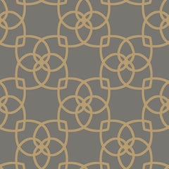 The Serendipity Wallpaper by York Wallcoverings features a symmetrical, seamless pattern of interlocking gold geometric shapes forming a floral motif on a dark gray background, creating a modern and decorative look.