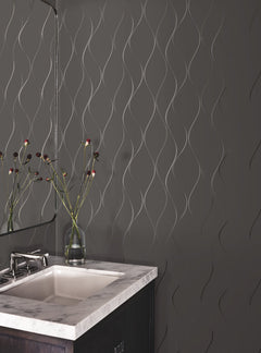 A modern bathroom features a marble countertop sink, a glass vase with flowers, a mirror, and a dark wall adorned with York Wallcoverings’ Wavy Stripe Wallpaper.